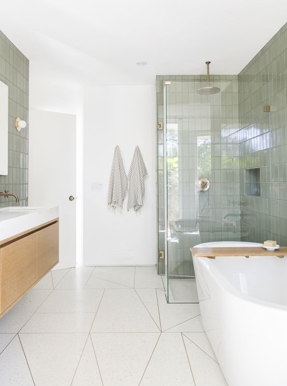An airy mid century modern bathroom with white geo and green skinny tiles, a floating vanity and a tub, a shower space