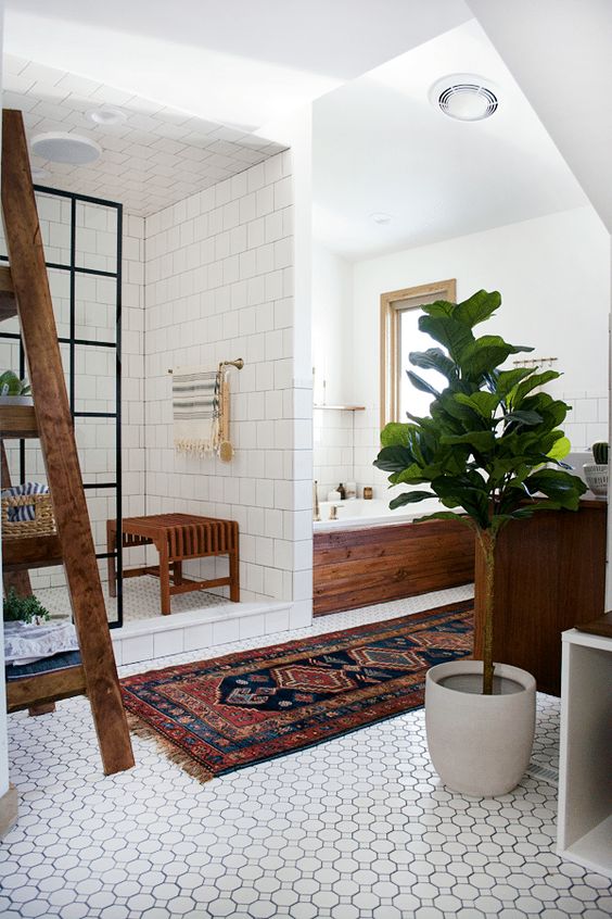 an attic boho bathroom with printed and square white tiles, a wooden stool, a tub clad with wood, a ladder and potted plants