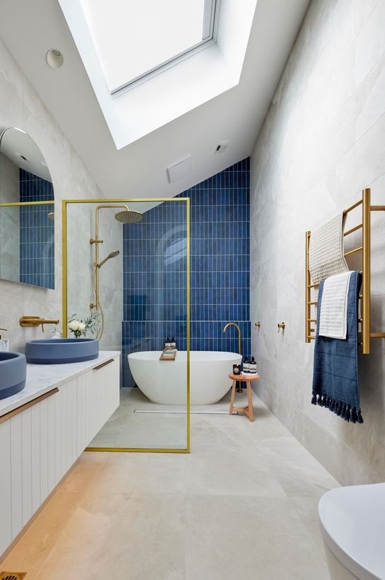 An ocean inspired bathroom with a skylight, large format tiles, a navy accent wall, a floating vanity with navy sinks and gold touches