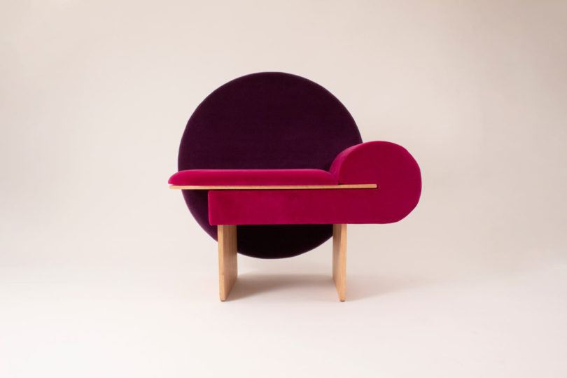 The base is made of wood, the chair is upholstered in hot pink and the back is a purple circle
