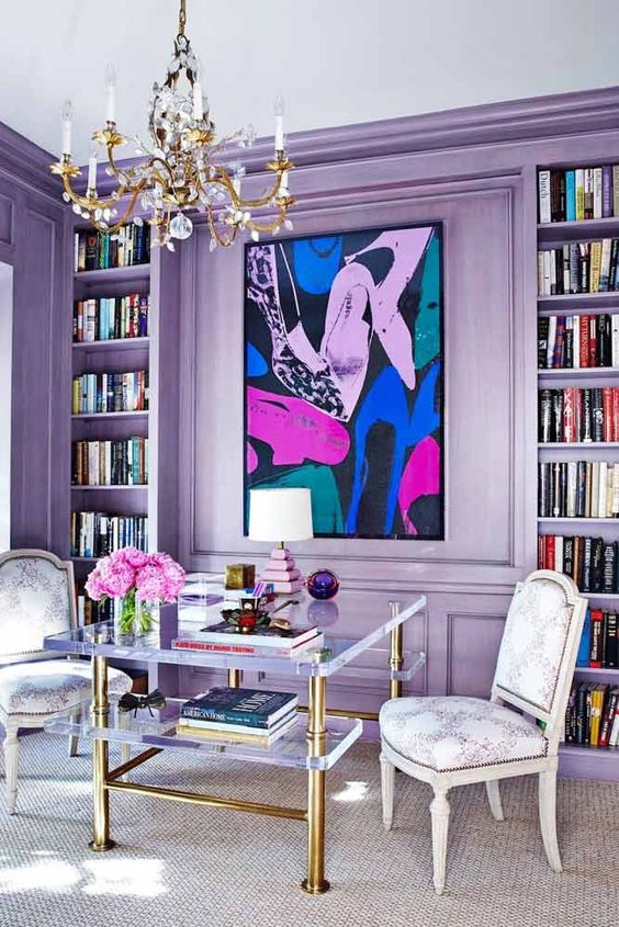 a bold glam living room with lilac walls and built-in shelves and a bright artwork is filled with tender colors