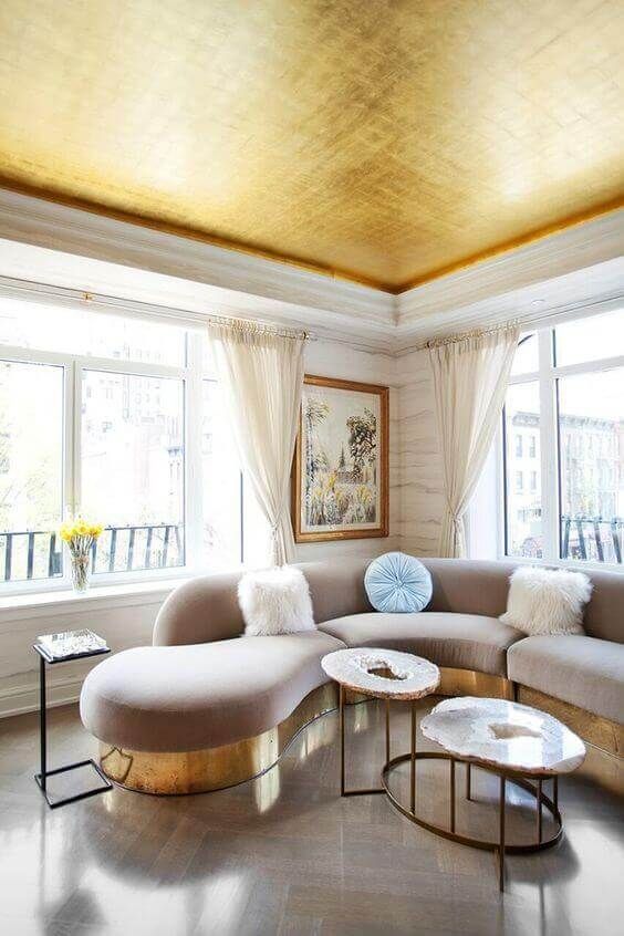 a chic and refined living room with elegant curved furniture and a gold ceiling that echoes the furniture base