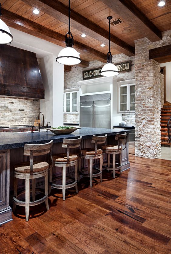 A rustic kitchen with a rich colored wood floor and whitewashed vintage wooden chairs