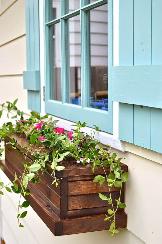 A stained slatted wood window box with fresh flowers adds interest to the light blue shutters