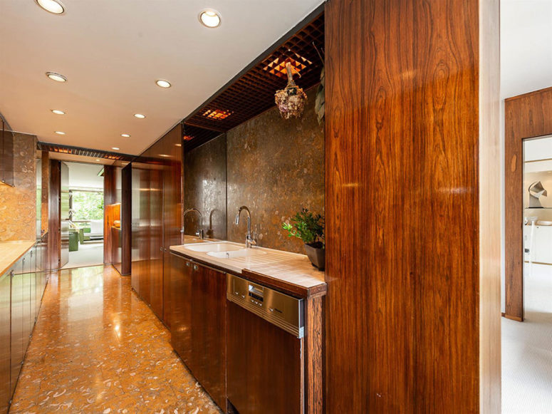The kitchen is done with modern rich-colored wooden cabinets and stone surfaces here and there