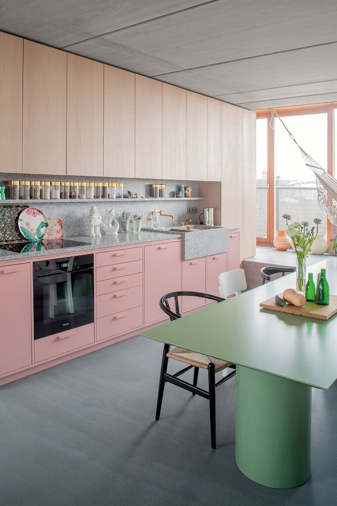 The kitchen is done with wooden and pink cabinets and a terrazzo countertop and backsplash