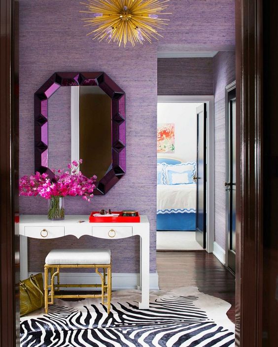 a bright entryway with lilac wallpaper walls and a purple mirror, gold touches add a glam feel to the space