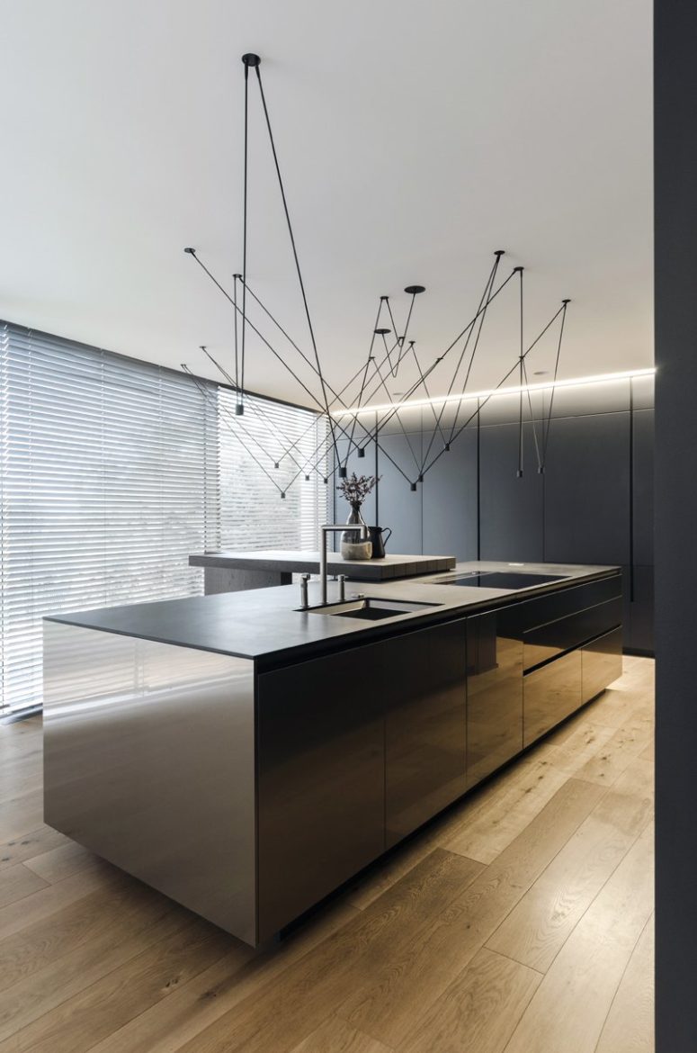 The kitchen is a dark and sleek one, with large cabinets and an oversized kitchen island with a breakfast space and suspended lamps