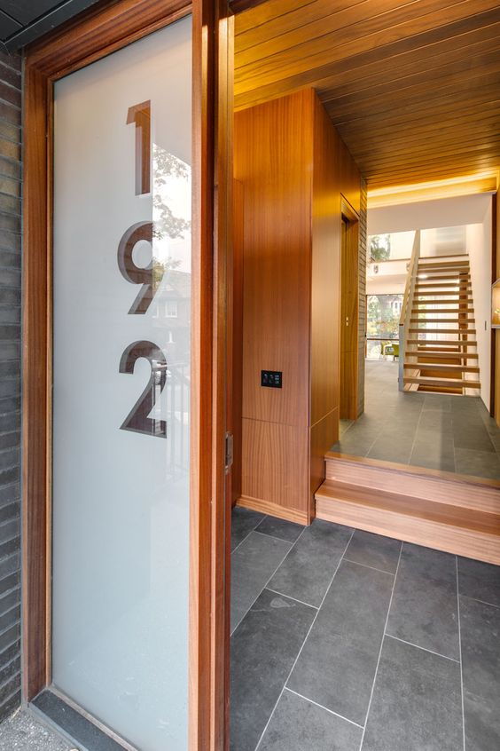 this front door, with an adjacent large glass panel showcasing the house number, guides visitors into the home