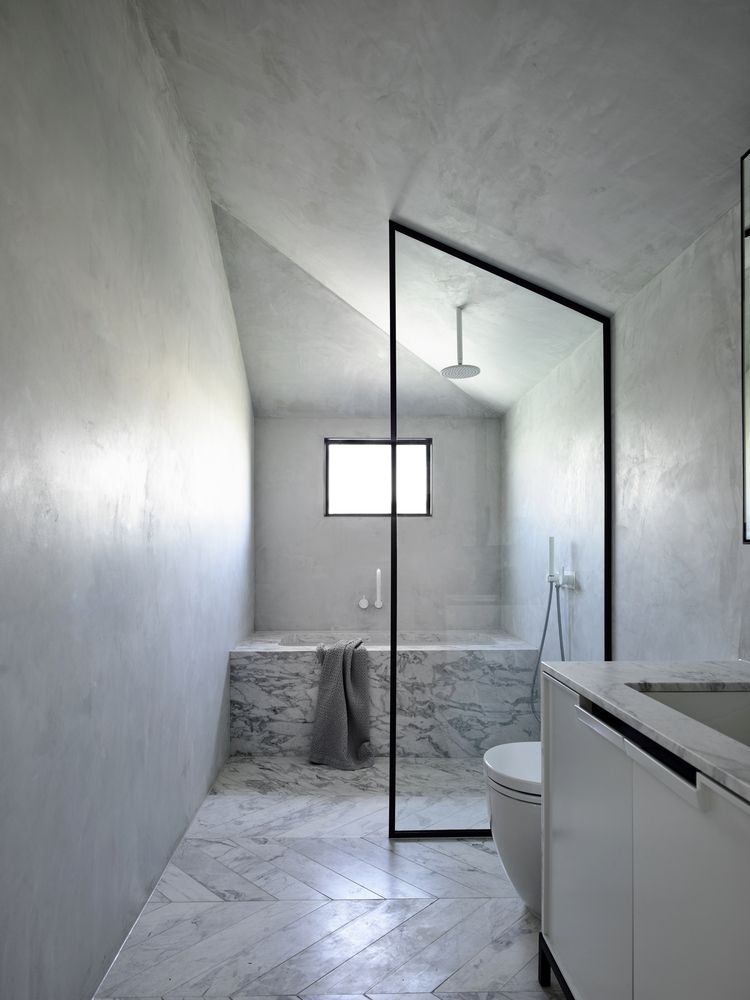There's a large marble clad bathtub and cocnrete walls plus a window that brings light in