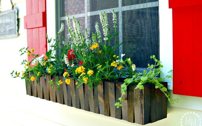 a dark stained picket fence flower box with colorful blooms is a bold idea and red shutters add to the look