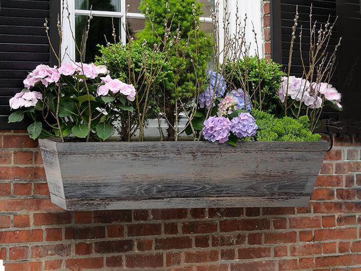a distressed wood window box with pastel blooms and foliage adds a cozy feel and traditional touch
