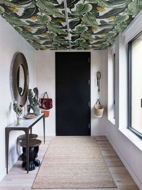An entryway with a bright ceiling covered with tropical leaf print wallpaper that adds color and print to the space