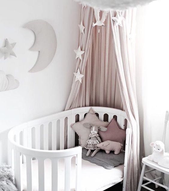 a curved crib with a blush canopy, pillows and stars for a beautiful girl's nursery