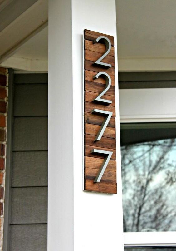 A stylish modern house number display with rich colored wooden planks and modern numbers attached to the corner of the house