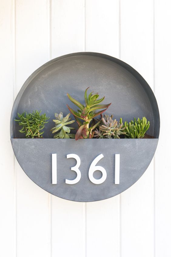 a brushed metal round wlal planter with numbers and succulents in it is a chic idea with a mid-century modern feel