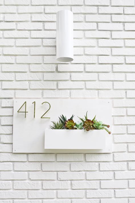 a chic white wall planter with succulents and numbers on a white brick wall is a stylish idea