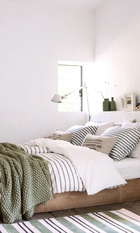 stripes, industrial prints on the pillows and a crochet green blanket create a fresh and spring-ready bed