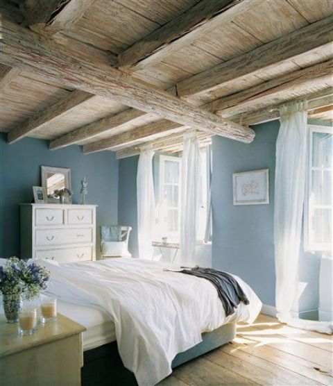 A vintage inspired bedroom with a rough and rustic wooden ceiling with lots of beams that takes over the space