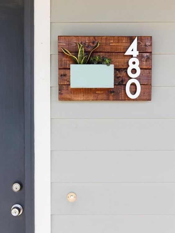 a wooden sign of stained planks, stylish numbers and some succulents in a pastel-colored planter