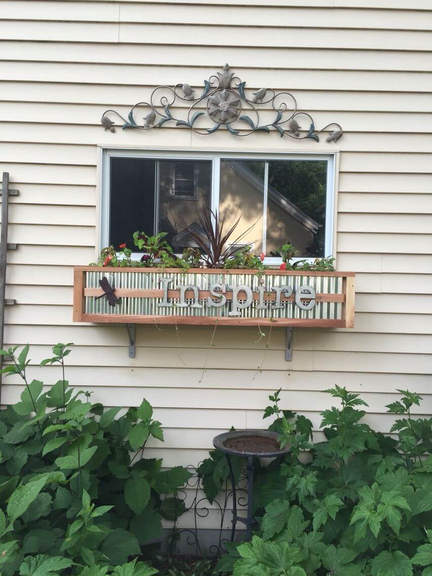A DIY wood and tin window box planter with greenery and other plants and some letters