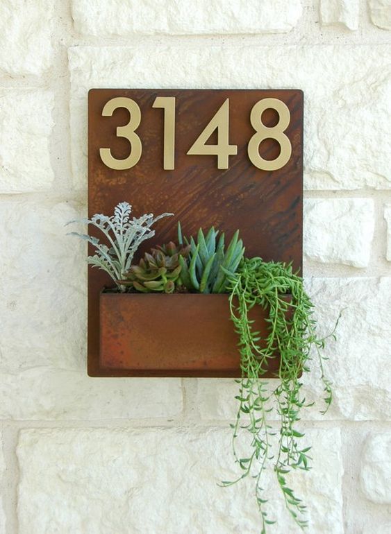 an aged metal outdoor wall planter with brass numbers and succulents and cascading greenery for a bold look
