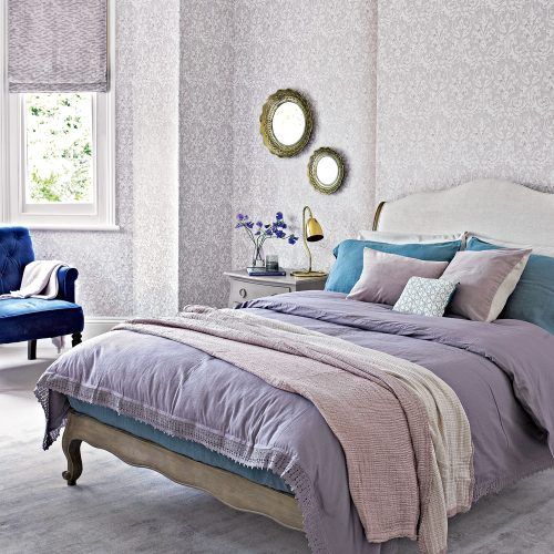 printed lilac wallpaper and Roman shades bring a vintage feel to the space, and lilac bedding helps with that