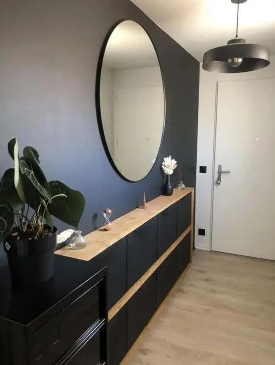 a boho entryway with a black wall and a black Trones cabinet with wooden countertops, a round mirror and a black shelf