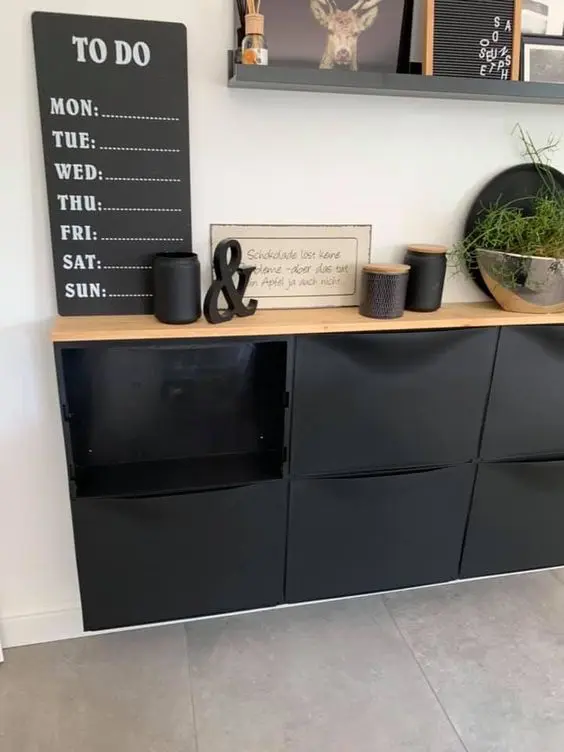 a cool space with a black Trones cabinet with a wooden countertop, a list, some black candles, greenery and a shelf with decor