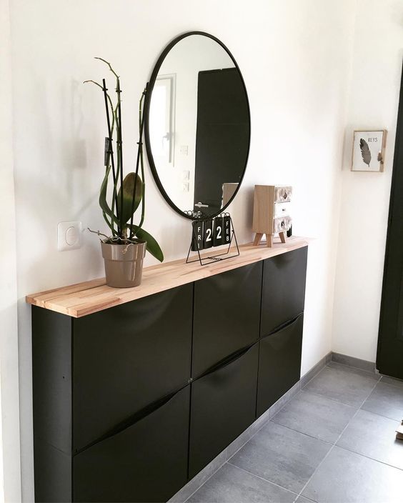 a modern entryway with a black Trones cabinet with a butcherblock countertop, a potted orchid, a round mirror and some decor