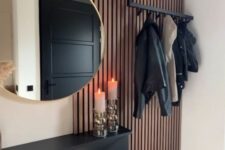 a modern entryway with a black Trones piece, a rack, a round mirror and a wooden slat accent