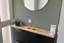a small and stylish entryway with an olive green wall, a black Trones cabinet with a wooden countertop, a potted plant and a round mirror