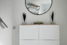 a small nook with a white Trones piece with built-in lights and a wooden countertop, a round mirror, grasses and gold birds