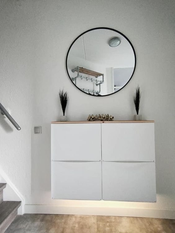 A small nook with a white Trones piece with built in lights and a wooden countertop, a round mirror, grasses and gold birds