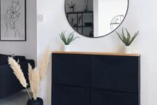 a stylish boho space with a black Trones cabinet with a wooden countertop, a round mirror, a black vase with pampas grass and potted plants