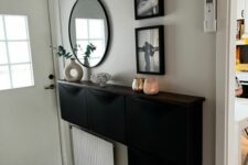 a stylish modern entryway with a black Trones and a radiator, black and white photos, a round mirror and some candles