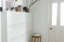 an airy space with a white Trones piece with vases, artwork and various decor, a wooden stool and a fluffy pendant lamp