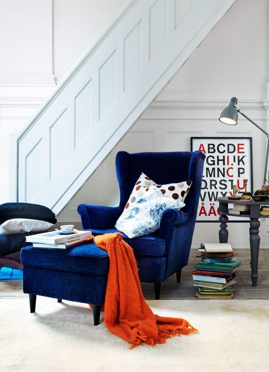 a navy velvet wingback chair with a matching ottoman and some colorful pillows for comfortable reading