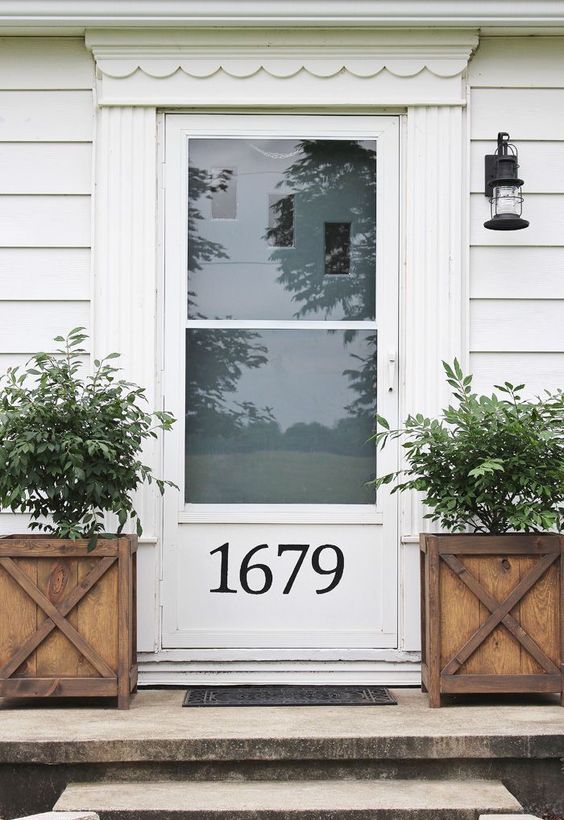 a white door with glass and a house number plus wooden planters and small trees for a vintage farmhouse feel