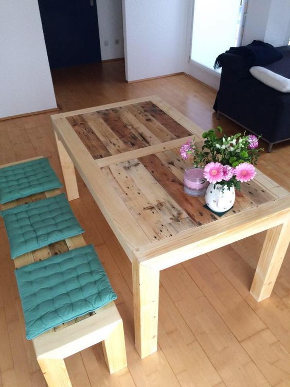 a light-colored stained dining table of pallet wood and matching benches with colorful cushions