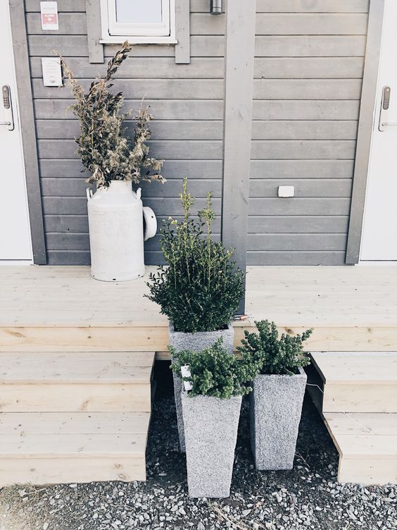 stylish concrete planters with greenery and a milk churn with some branches for a modern front yard