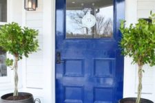 08 a cobalt blue front door and striped planters with small trees and a jute rug for a bright and welcoming porch