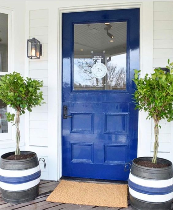 a cobalt blue front door and striped planters with small trees and a jute rug for a bright and welcoming porch