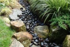 08 a dry creek bed with dark pebbles and lined up with large rocks and grasses is a cool idea