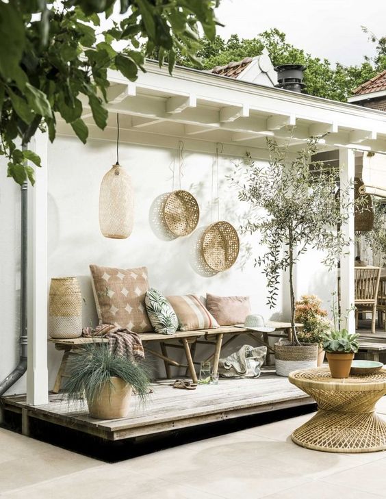 a welcoming boho tropical patio with a rattan table, a wooden bench with plenty of pillows, wicker planters and decorative baskets