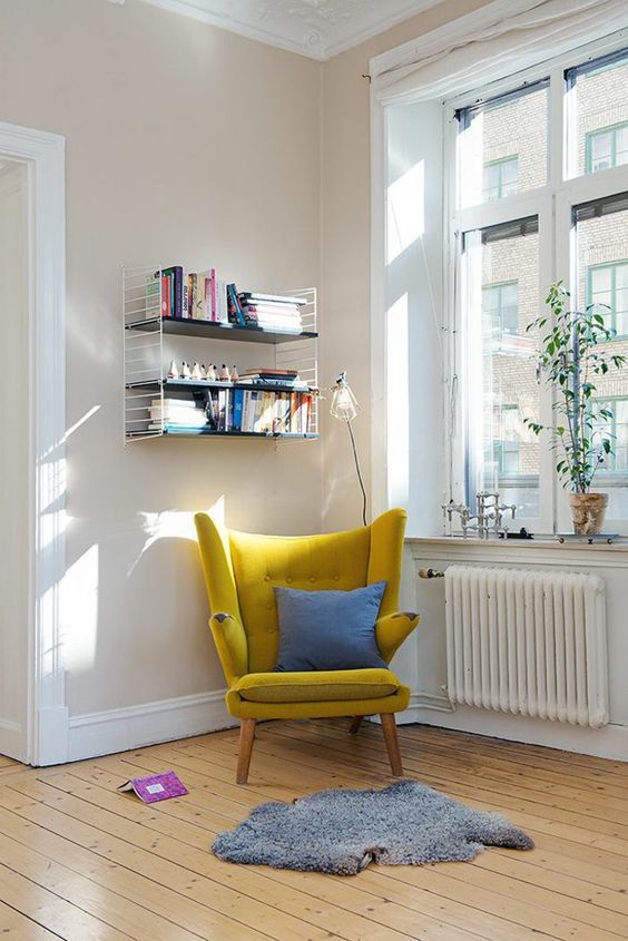 a mustard wingback chair with a blue pillow and a grey rug by the window is a cute idea