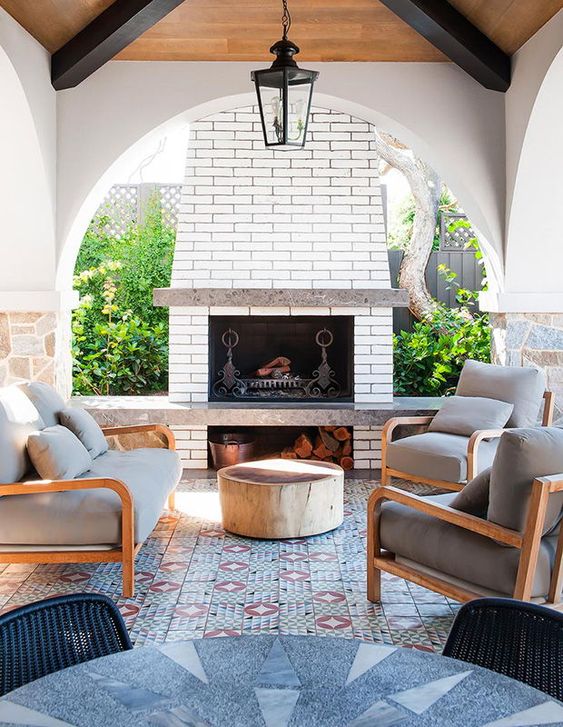 a bright outdoor lounge with a fireplace, a mosaic tile floor and a bold table plus comfy chairs