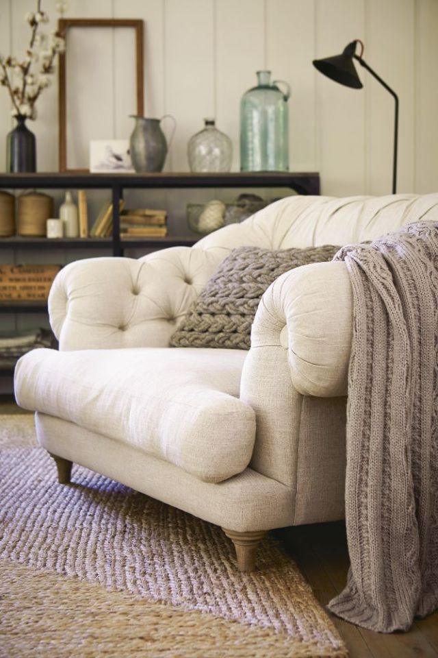 a gorgeous large overstuffed chair in cream, with wooden legs and a knit blanket and pillow to sink in