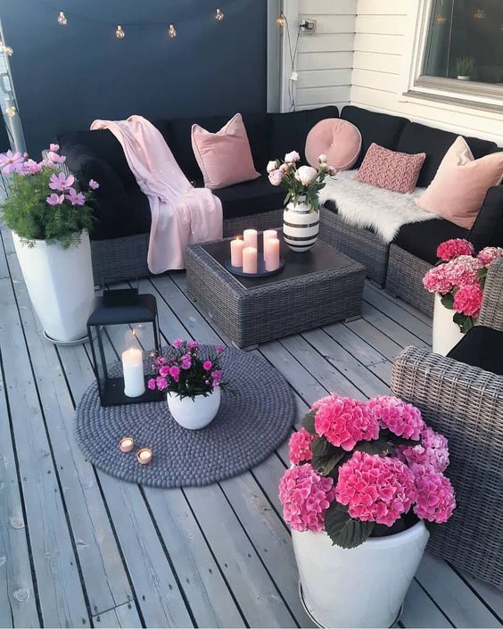 a bright black and blush deck with wicker furniture, blush pillows and hot pink potted blooms