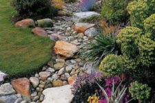 13 a dry river bed with pebbles and larger pieces of rocks and grass and bright blooms lining up